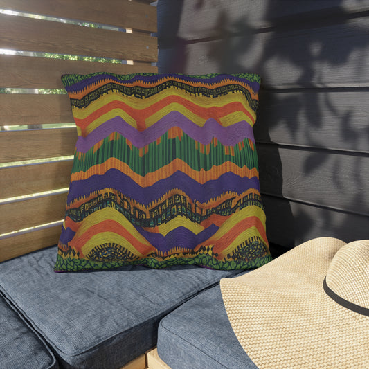 A square outdoor pillow with a bold, multicolor zigzag pattern in green, orange, purple, and yellow—crafted from water-resistant fabric—rests on a blue cushioned bench beside a straw hat. Wooden slats cast leafy shadows in the sunny setting.