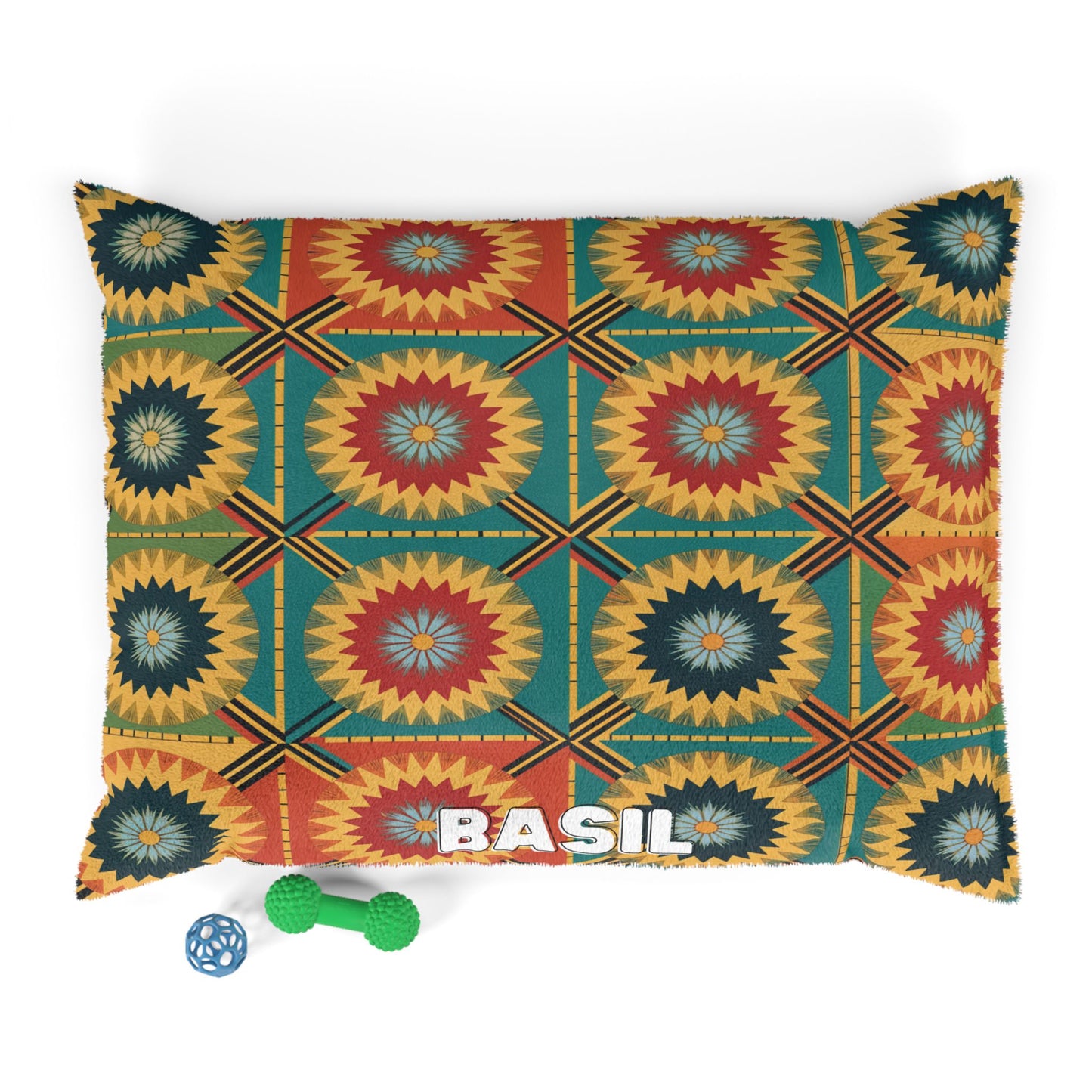 A rectangular dog bed with a colorful geometric sunburst pattern in yellow, teal, orange, and blue offers luxurious comfort. BASIL is written in white on one corner. Next to the bed are two dog toys: a green bone and a blue lattice ball.