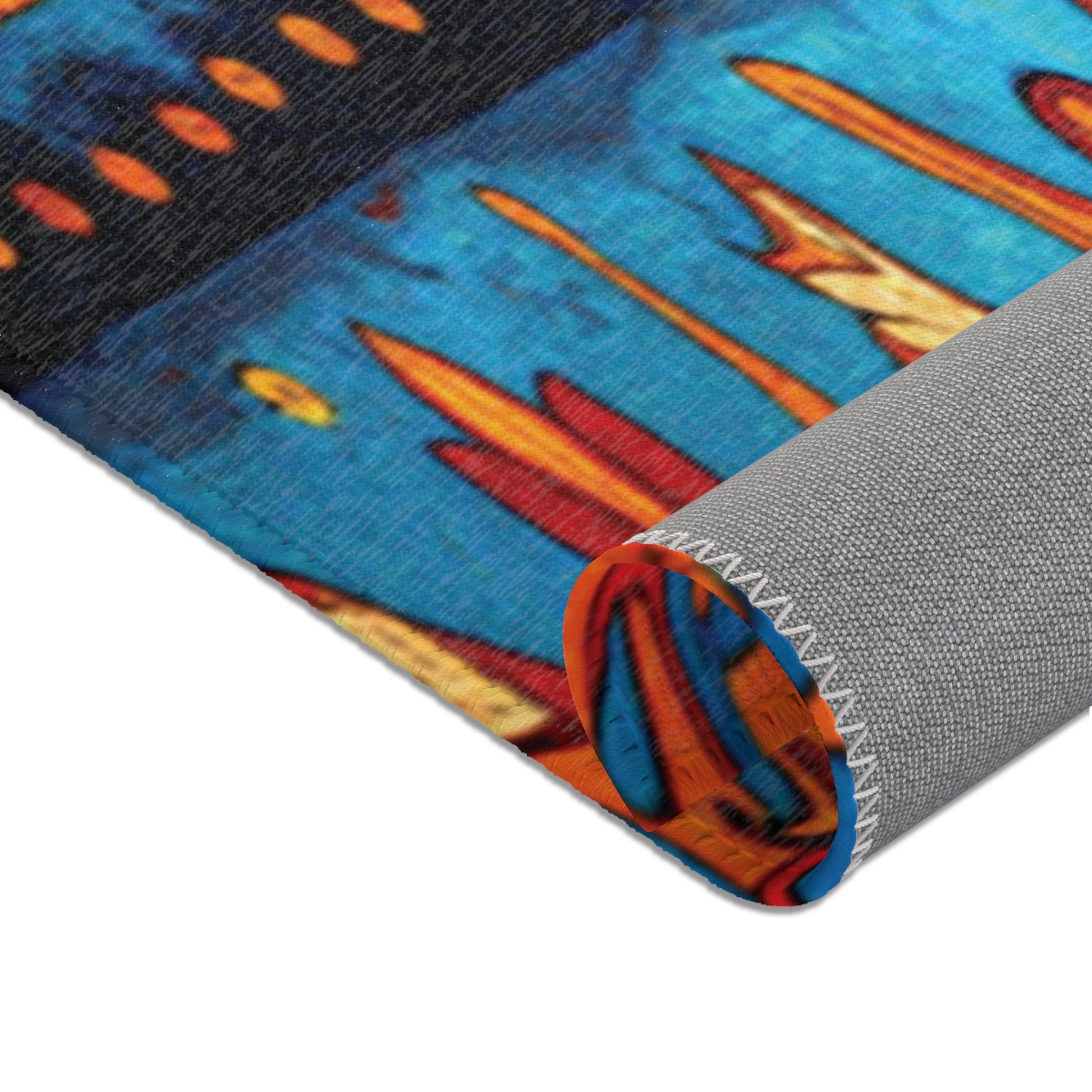 A close-up of a rolled-up rug displays a vibrant geometric pattern in blue, orange, yellow, and black. Featuring stylish colorful rugs’ flair, its edge has white stitching and a textured light gray backing with elongated shapes and dots in the design.