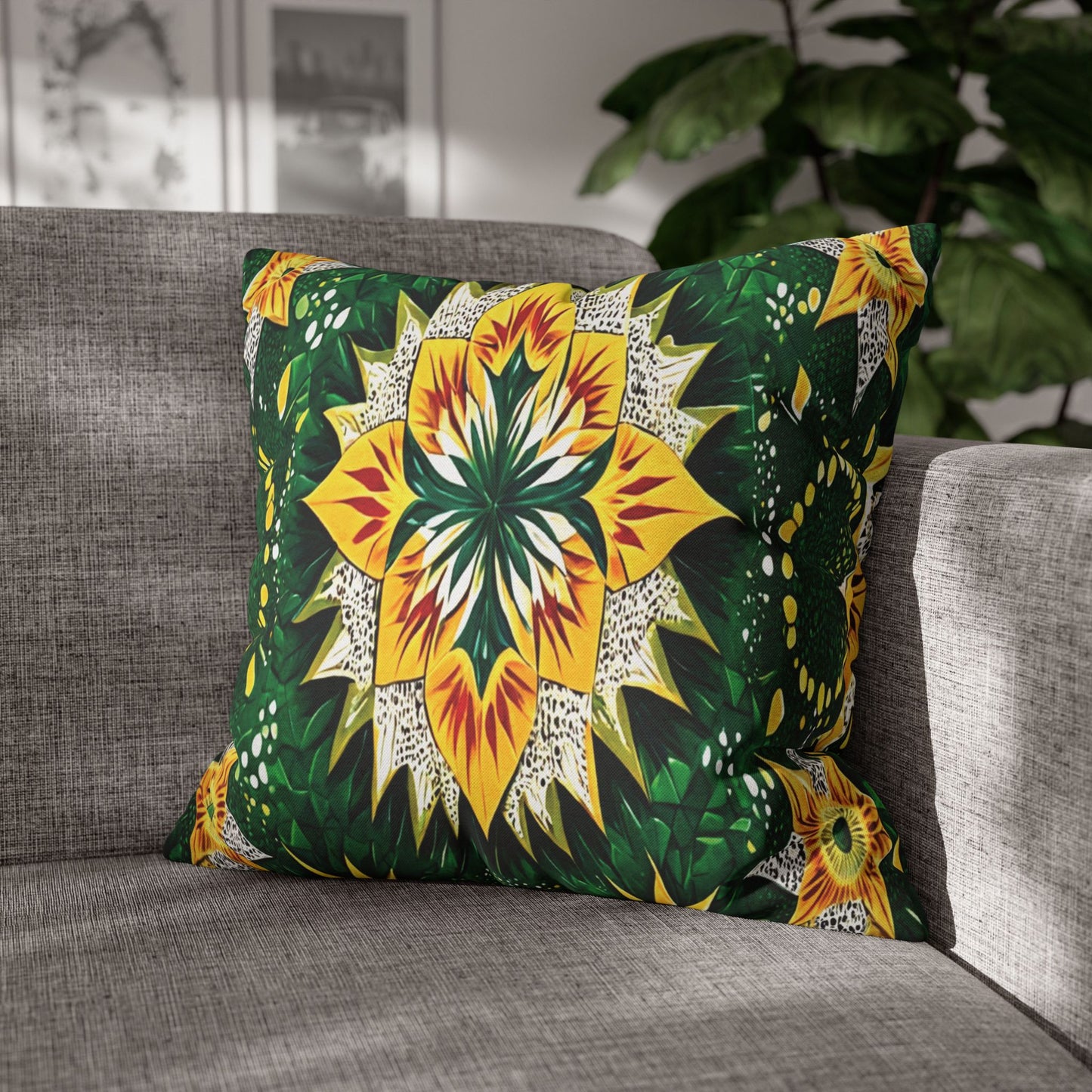 A square pillow with a bold, symmetrical floral design in yellow, green, and white rests on a gray fabric sofa. Sunlight streams in, highlighting its African-inspired pattern. A leafy plant and framed art are blurred in the background.