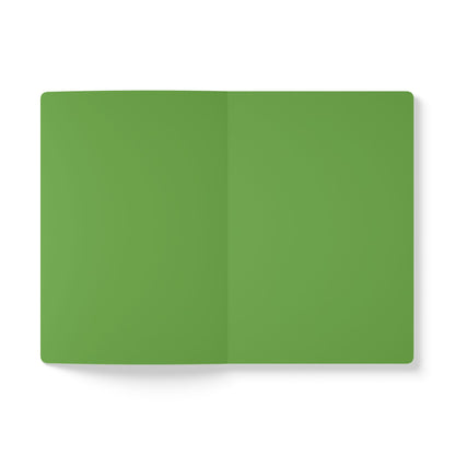 An open, blank African-inspired journal with green pages lies flat on a white background. The notebook’s center fold is visible, its edges are rounded, and the pages are perfect for creative journaling. The lighting is even and soft.