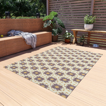 A cozy patio with wicker furniture, potted plants, and a patterned rug featuring African-inspired purple flowers on a light background. A plaid blanket is draped on the sofa, while sunlight filters through a slatted privacy screen behind the scene.