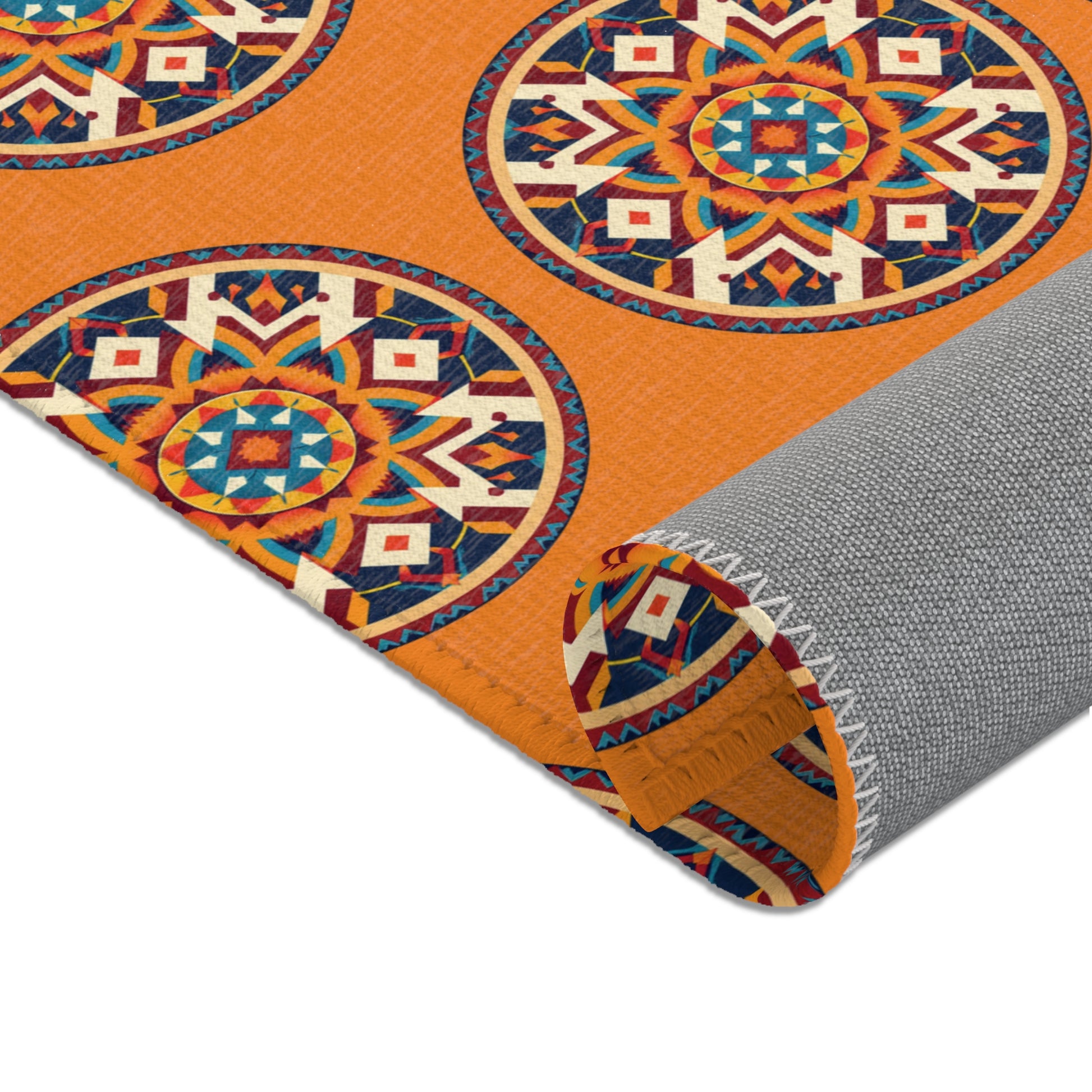 A rolled-up mat with a vibrant orange background features large, circular geometric patterns in red, blue, yellow, and white. The African-inspired design creates a bold and lively look, while the mat’s gray underside has a textured finish.