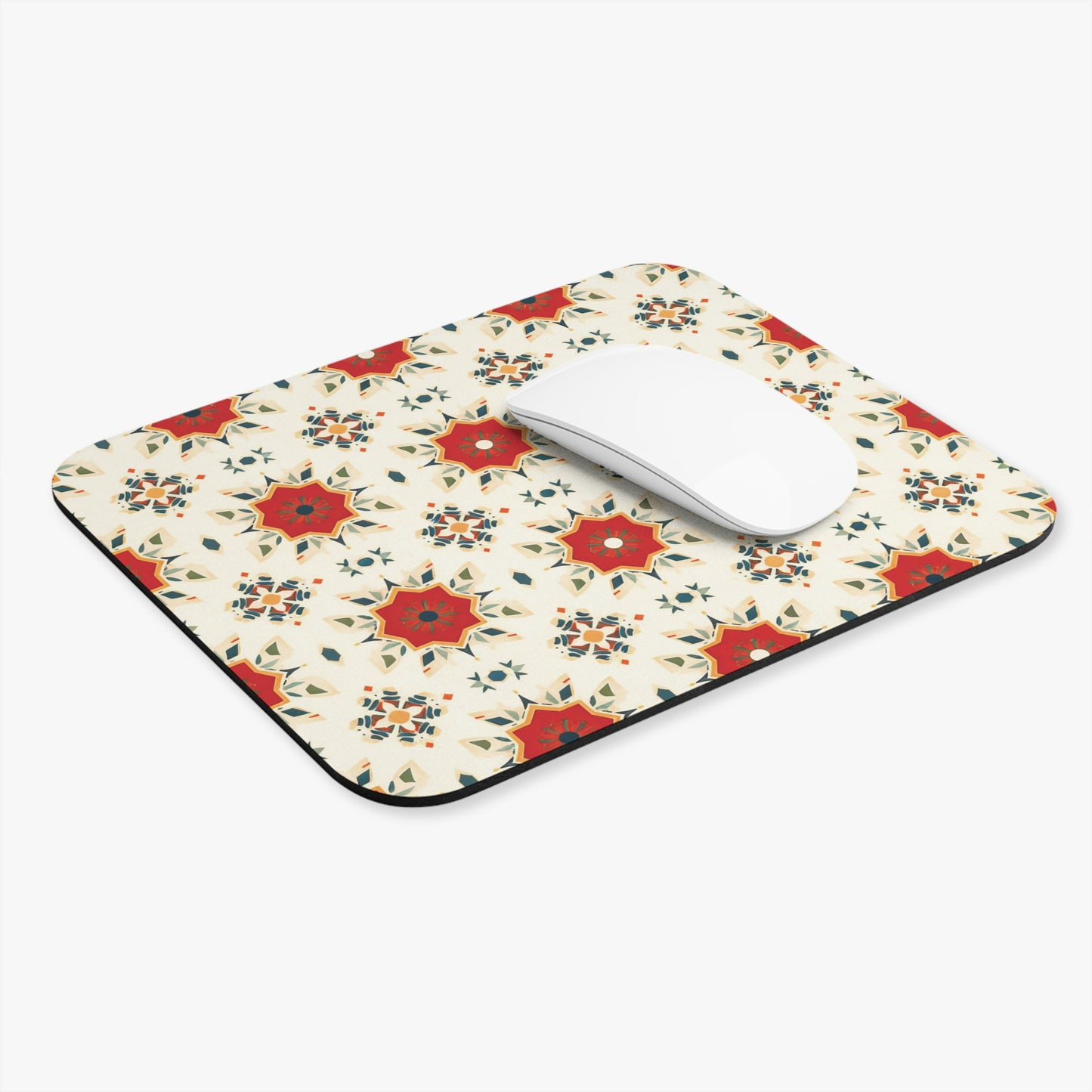 A rectangular, African-inspired mouse pad with a repeating pattern of red, gold, and blue geometric star shapes on cream. A white, curved wireless mouse sits on top, highlighting this vibrant desk accessory against a plain white background.