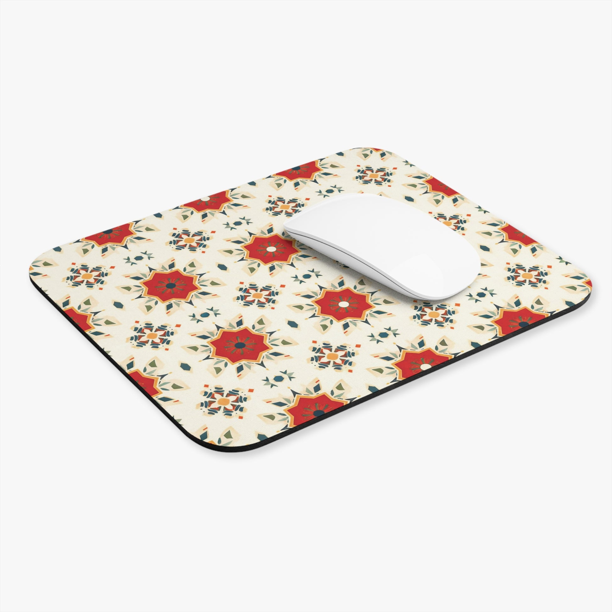 A rectangular, African-inspired mouse pad with a repeating pattern of red, gold, and blue geometric star shapes on cream. A white, curved wireless mouse sits on top, highlighting this vibrant desk accessory against a plain white background.