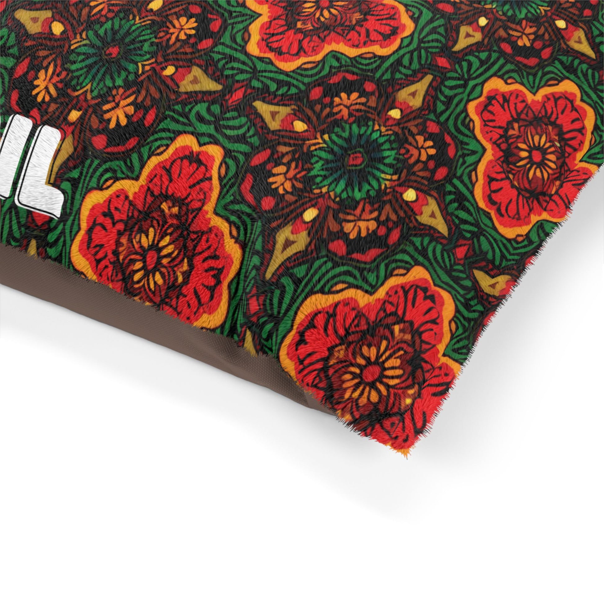 A close-up of a pillow corner with a vibrant, African-inspired floral pattern. The design includes large red and orange flowers with green leaves set against a dark background. Part of a white, bold letter appears on the left side.