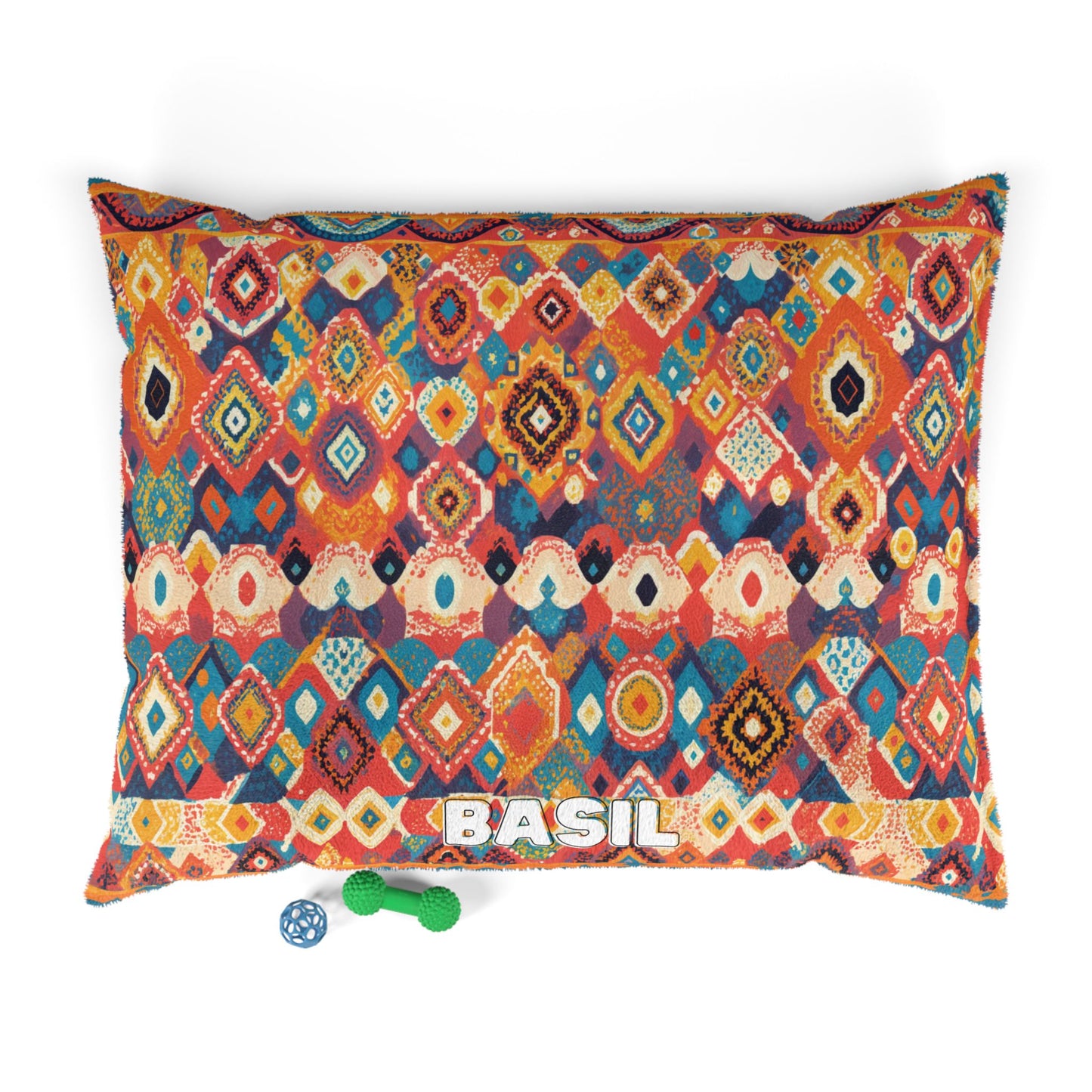 A colorful rectangular dog bed with an African-inspired geometric tribal pattern in red, orange, blue, and yellow hues. The name BASIL is printed in bold white letters at the front. Two dog toys, a blue ball and a green bone, lie nearby on a white background.