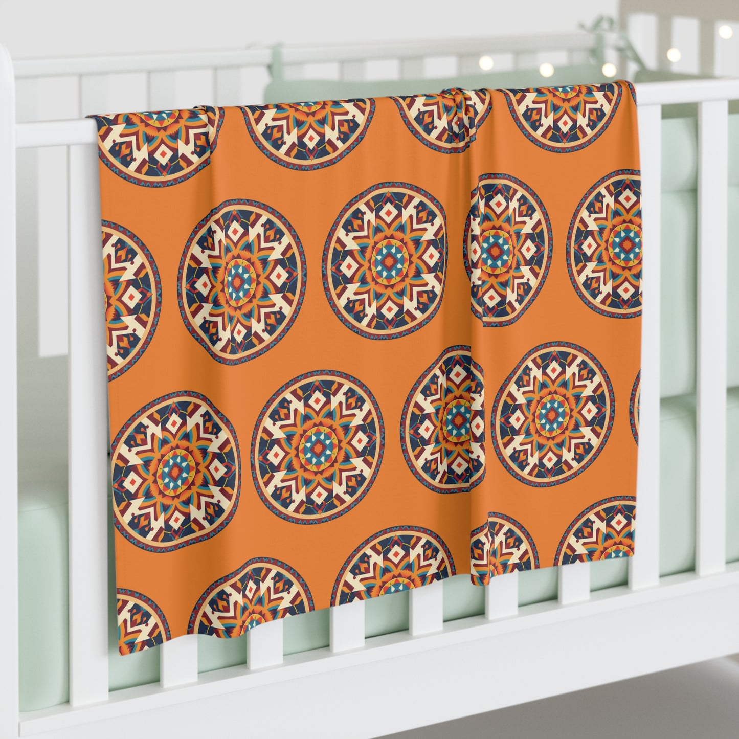 A white crib with mint-green bedding is adorned with a soft baby blanket draped over the side, featuring colorful, mandala-like designs on orange. Soft fairy lights twinkle in the background, adding to the African-Inspired decor.