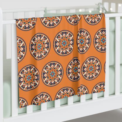 A white crib with mint-green bedding is adorned with a soft baby blanket draped over the side, featuring colorful, mandala-like designs on orange. Soft fairy lights twinkle in the background, adding to the African-Inspired decor.