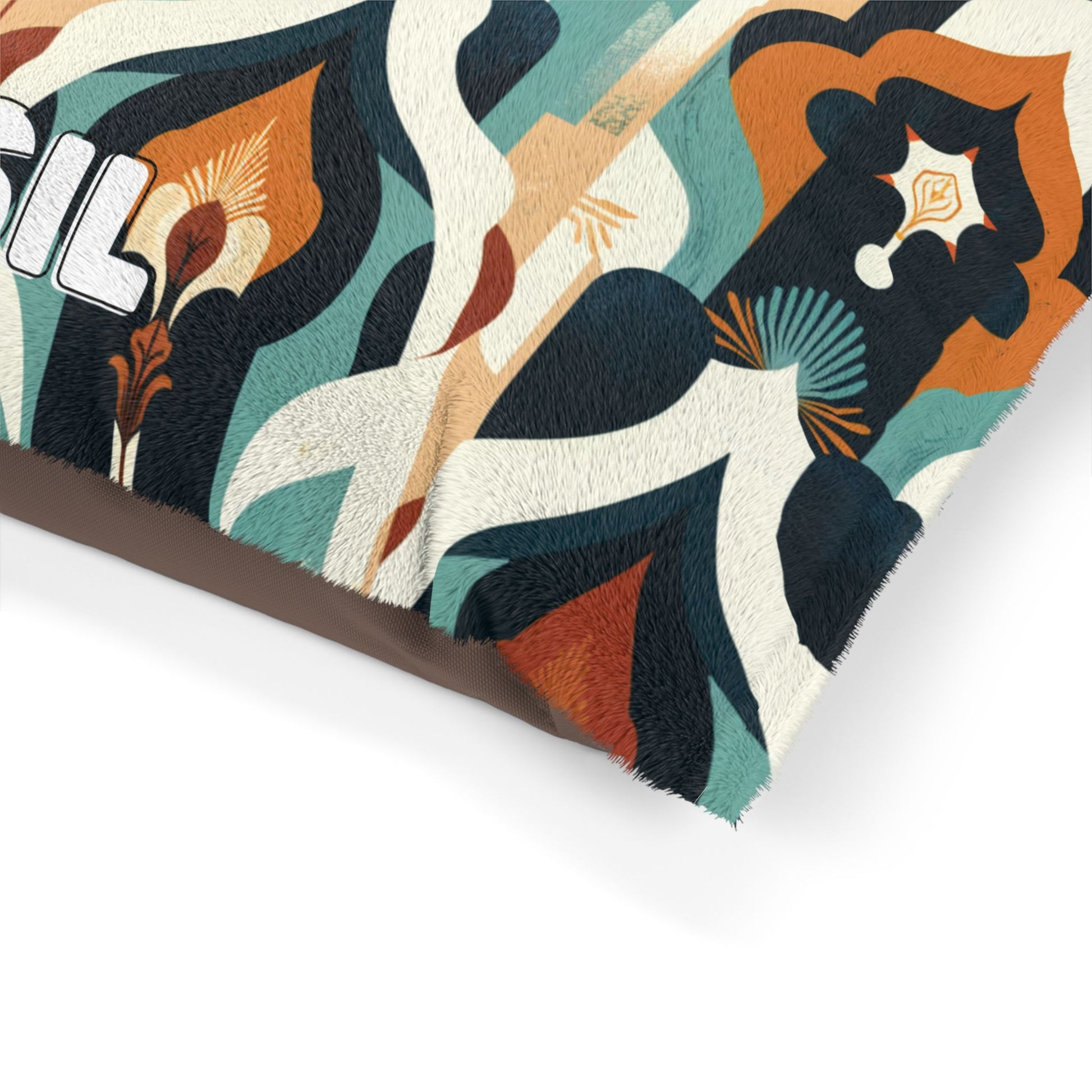 Close-up of a rectangular cushion with a vibrant, abstract pattern in teal, orange, cream, and black. The durable construction features bold shapes and stylized botanicals. The corner is visible, with text beginning with IL on the left.