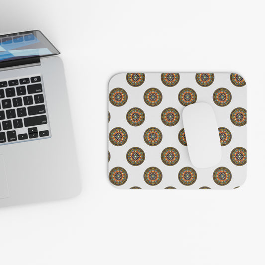 A silver laptop sits on a white surface next to a white mouse on an African-inspired mouse pad with colorful mandala designs. The laptop is partly open, showing a black keyboard and touchpad. The pad’s non-slip rubber base adds a creative desk accessory touch.