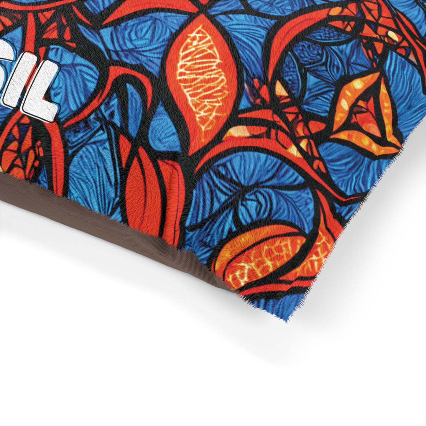 Close-up of a stylish pet bed pillow showcasing an abstract pattern in red, blue, black, and orange shapes resembling leaves and flames. The brown fabric edge and a partial view of the embroidered word BRASIL add unique flair.