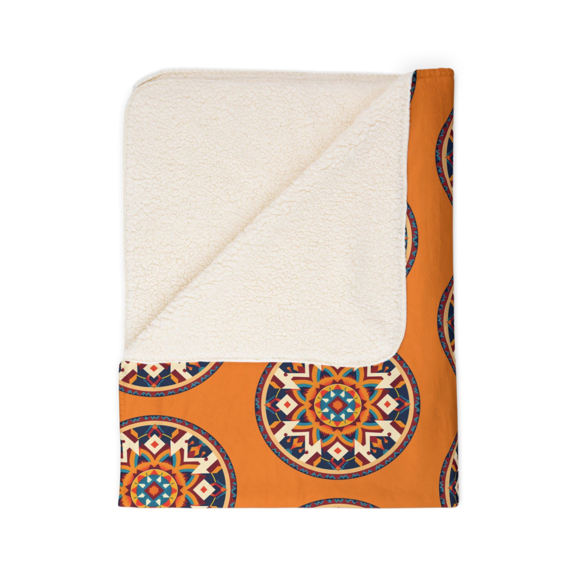 A folded blanket with a white, fluffy sherpa lining and a burnt orange fabric featuring African-inspired circular, colorful geometric mandala patterns. The corner is turned over to show the contrasting soft lining against a plain white background.