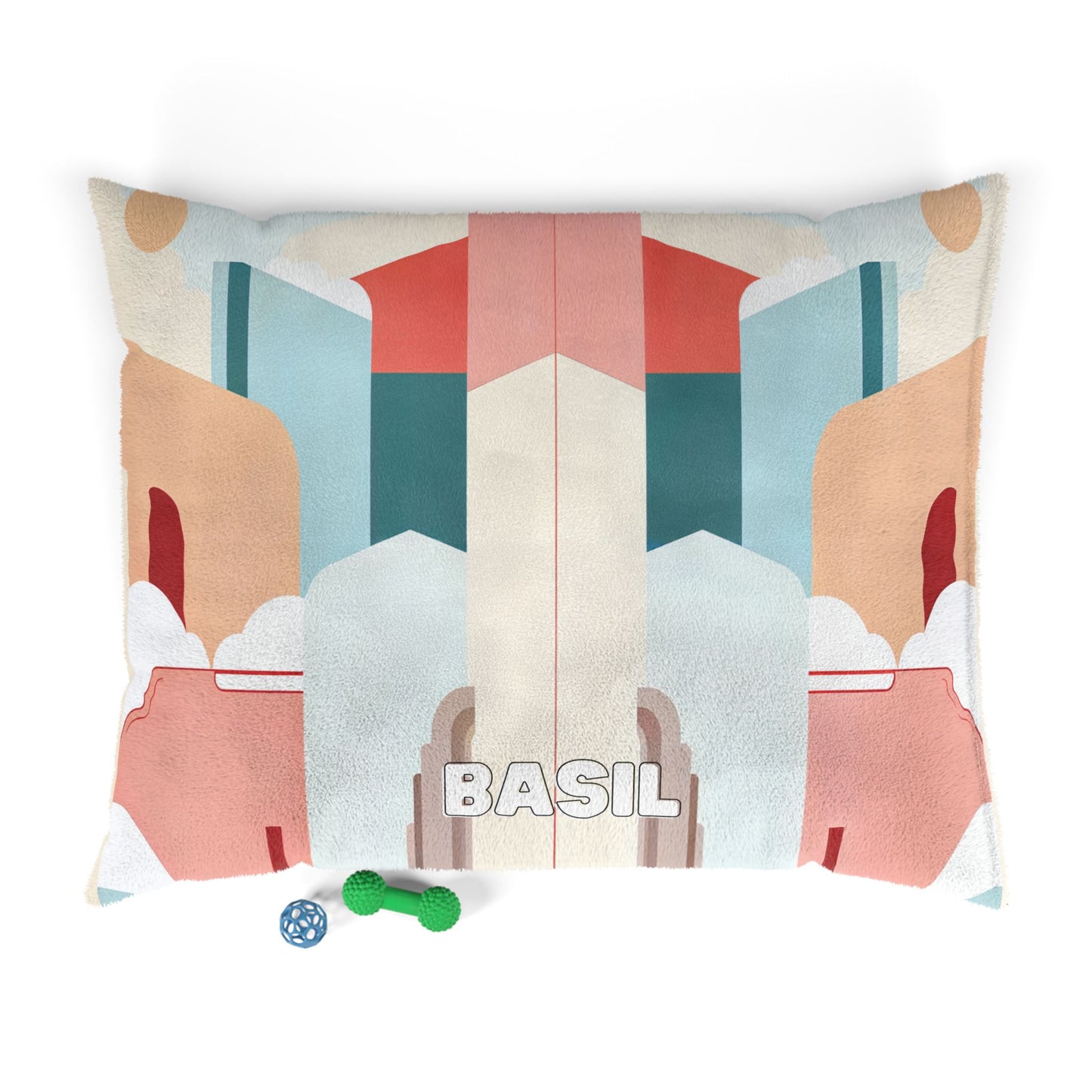 A rectangular dog bed with African-inspired geometric, pastel shapes in tan, teal, coral, and cream. The name “BASIL” is printed in bold white letters at the center. Two dog toys—a blue bone and a green textured ball—rest on the bottom left corner.