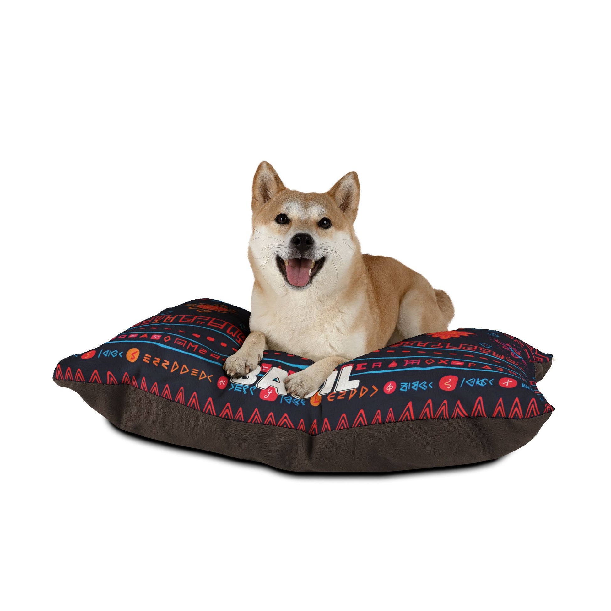 A Shiba Inu dog lies on a large, colorful personalized pet bed with geometric patterns in red, blue, and orange. The dog faces forward with its mouth open, appearing happy and relaxed against a plain white background.