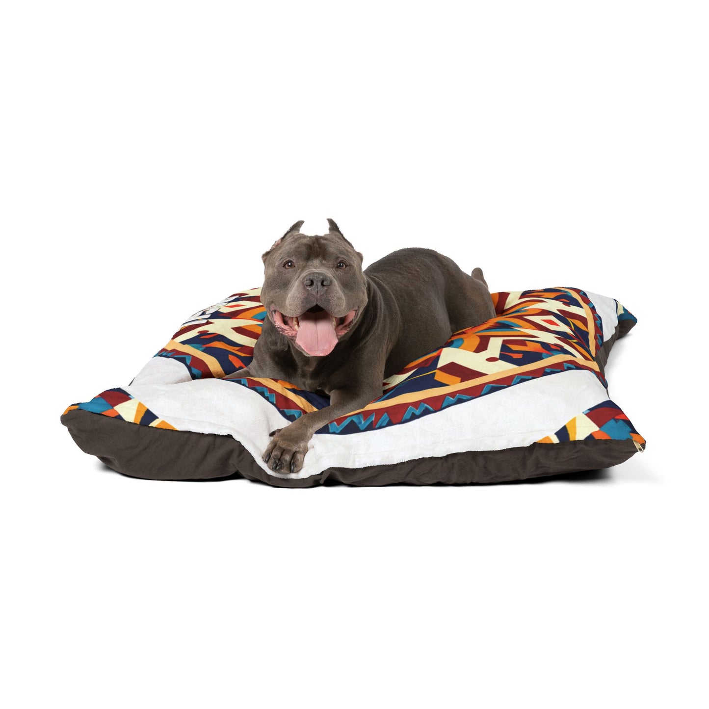A gray pit bull with cropped ears lies on a colorful, geometric-patterned dog bed, enjoying luxurious comfort. The dog faces the camera, mouth open and tongue out, looking happy and relaxed. The background is plain white.