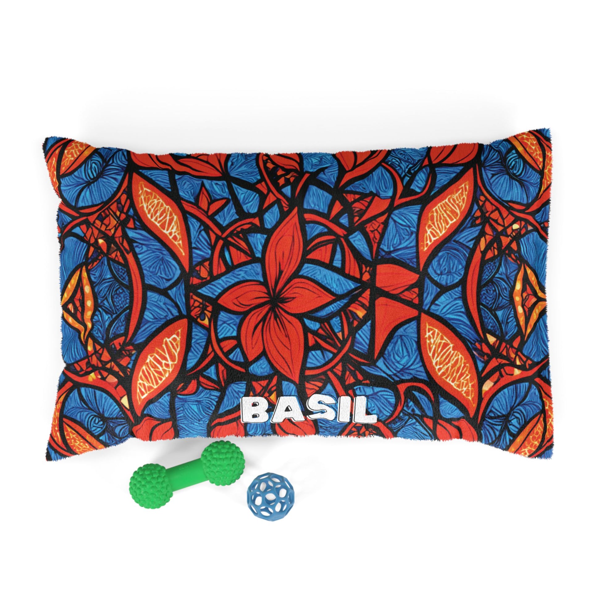 A cozy, African inspired pet bed with BASIL in bold white letters at the bottom center. Its vibrant pattern in red, blue, orange, and black stands out, while two dog toys—a green textured bone and a blue ball—sit in front.
