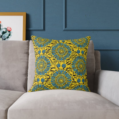 A colorful accent pillow with a vibrant yellow background and blue circular floral patterns sits on a light gray sofa. The wall behind is dark blue with decorative molding, and part of a framed cactus artwork is visible on the left.