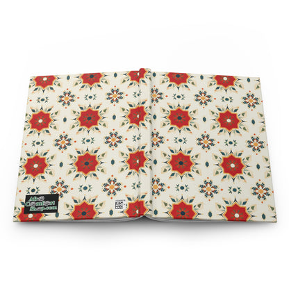 A hardcover journal is shown open, featuring a cover with a repeating geometric pattern of red and orange star shapes and blue accents on a cream background. A small black label reads Alice Coltrane blue-paint in white text on the front cover’s bottom left.