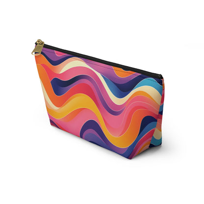 A zippered T-bottom pouch with a bold, colorful wavy pattern inspired by African-inspired patterns in shades of orange, pink, red, yellow, purple, and blue. Perfect as a cosmetic travel bag, it stands upright with a black zipper and gold zipper pull.