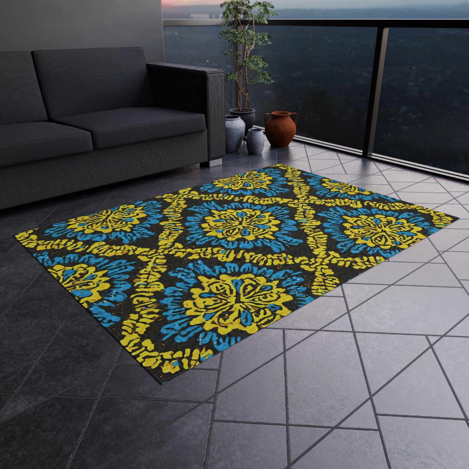 A modern balcony features a gray sectional sofa, an African-inspired outdoor rug with blue-and-yellow ornate patterns, two clay pots with leafy plants, and dark tiled flooring. A glass railing offers a cityscape view at dusk.