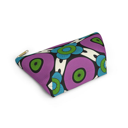 A triangular cosmetic travel bag with a gold zipper, featuring African-inspired patterns in bold florals. Large purple shapes and green-blue circular flowers pop on a white background with black accents. The T-bottom pouch rests on a white surface.