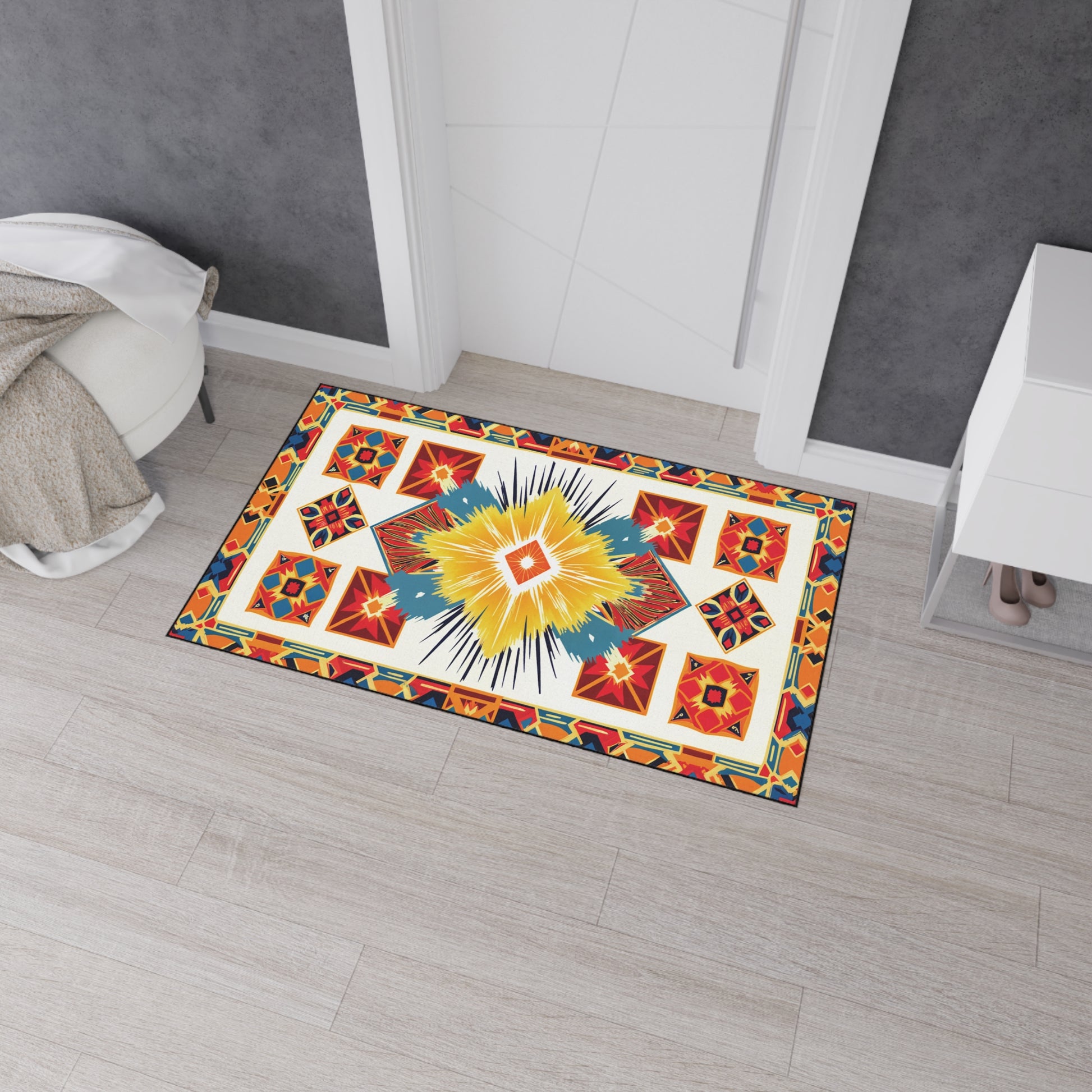 A rectangular rug with a vibrant geometric pattern, inspired by African-inspired floor mats, features yellow, red, blue, and black shapes. It lies on light wood flooring in front of a white door with a beige blanket draped nearby.