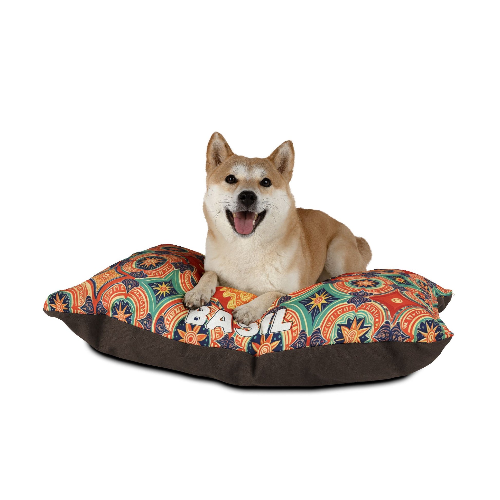 A happy Shiba Inu dog lies on a stylish pet bed with colorful geometric and floral patterns. The bed has a multicolored top and dark brown base, and the cheerful dog looks directly at the camera with its mouth open.