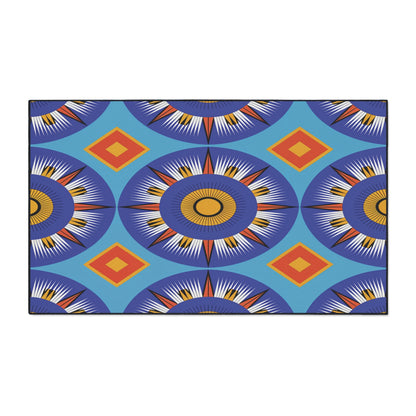A rectangular African-inspired floor mat featuring bold geometric patterns in blue, orange, yellow, and white. Large sunburst circles alternate with orange diamonds on a bright blue background. Includes a non-slip rubber backing for safety.