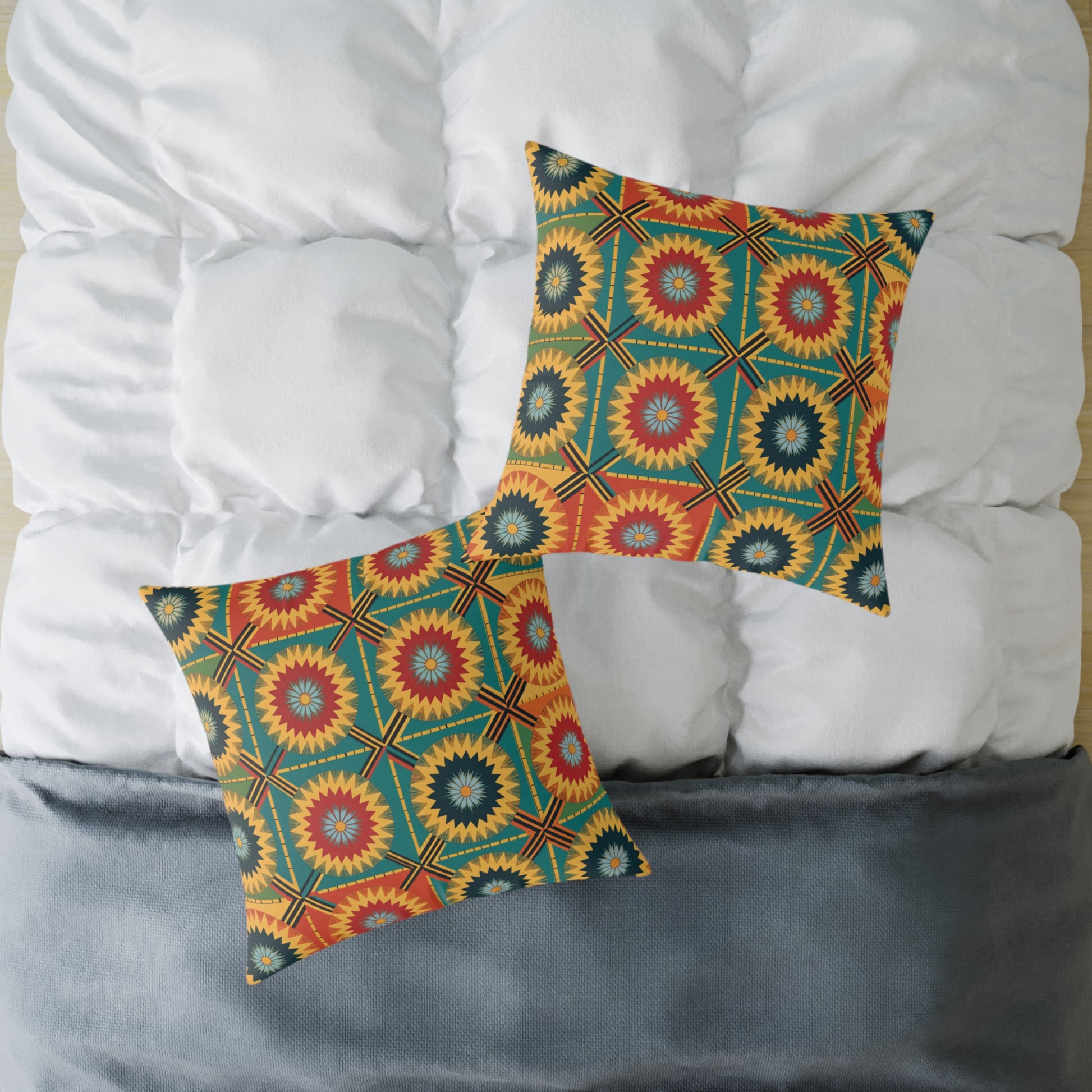 Two square, African-inspired pillows with a bold geometric pattern in red, yellow, and green rest on a white tufted comforter. The bed features a dark gray blanket at the foot, adding a touch of colorful home decor seen from above.
