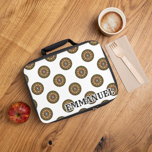 A personalized lunch bag, this white lunchbox features colorful circular patterns and the name EMMANUEL in bold black letters. It rests on a wooden table with a red apple, coffee with foam, and wooden utensils on a paper napkin beside it.
