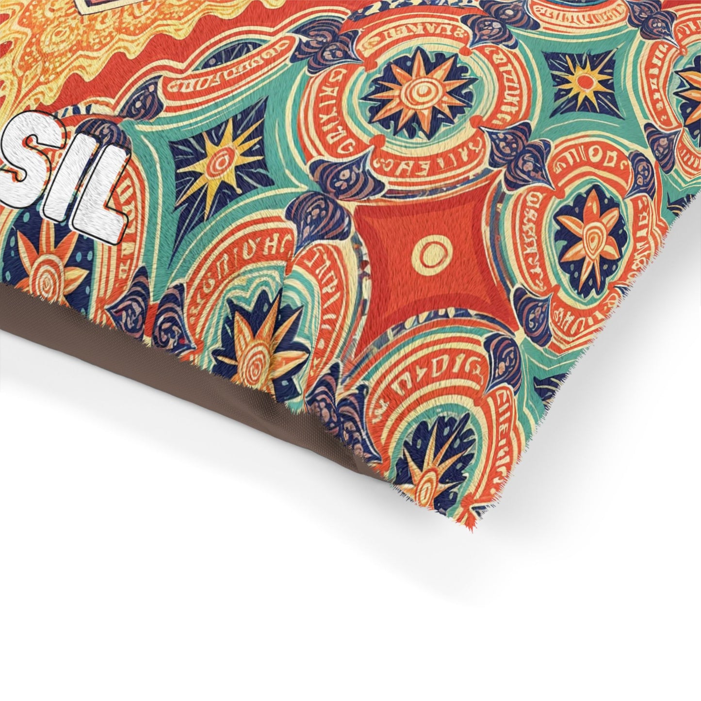 A colorful fabric with intricate, circular mandala patterns in orange, blue, green, and cream covers a cozy dog bed. The fabric features partial bold white text outlined in black on the left that reads SIL, while the edge is slightly frayed.