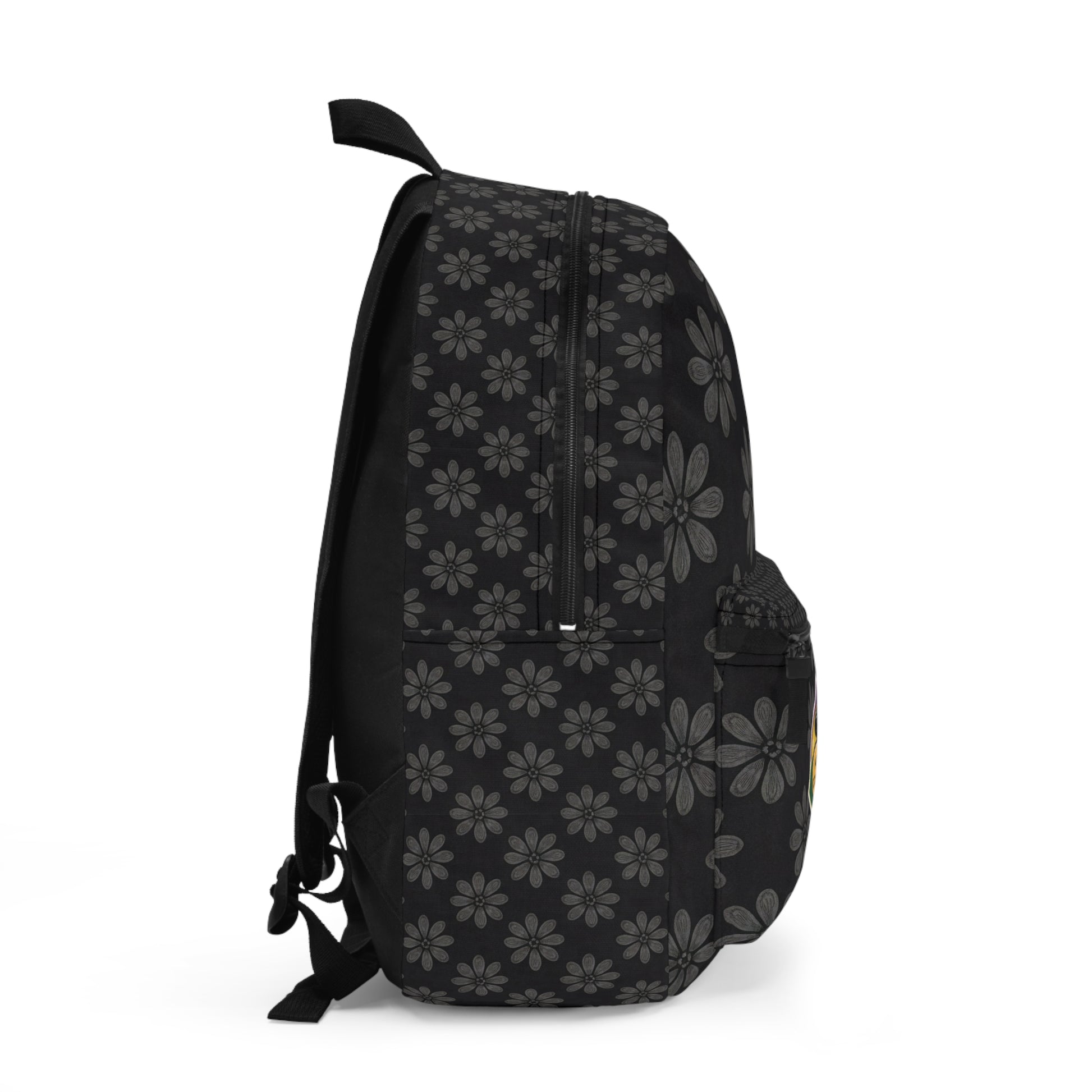 A black boho chic rucksack viewed from the side, featuring a repeating pattern of gray daisy-like flowers. The bag has a front pocket, mesh side pocket, zippers on top, and adjustable shoulder straps visible on the left. Plain white background.