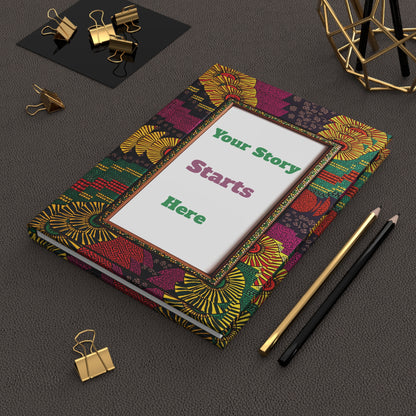 A colorful, African-inspired hardcover journal with a frame on the cover reads “Your Story Starts Here.” Set on a textured dark surface, it’s surrounded by gold binder clips, a gold wire decor piece, and black and gold pencils.