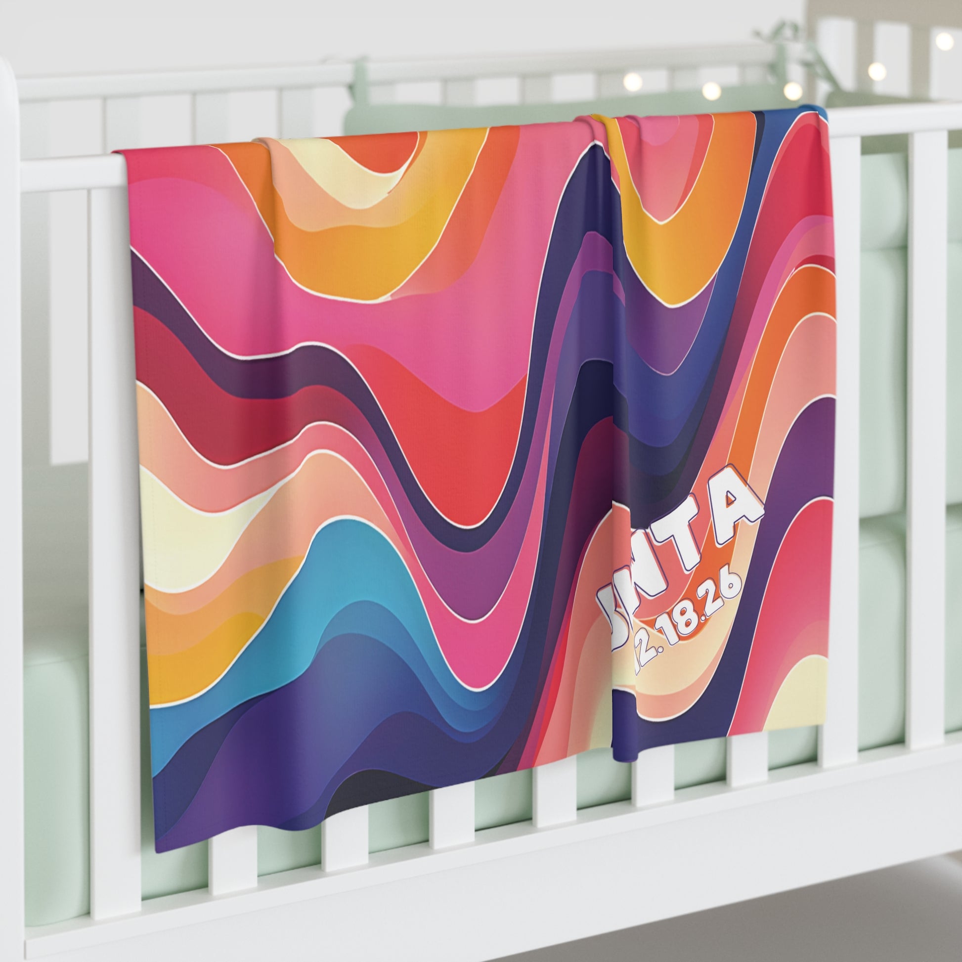 A colorful personalized baby blanket with bold, wavy lines in pink, red, orange, blue, and purple hangs over a white crib. This custom swaddle blanket features “JNT A 12.18.26” in the lower right corner—perfect for African-inspired decor.