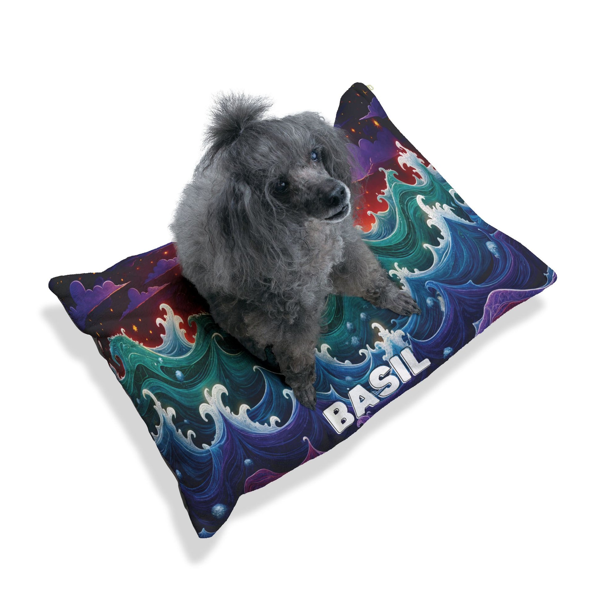 A gray poodle sits on a personalized pet bed—a colorful rectangular pillow with swirling blue, green, and purple waves, featuring BASIL in bold white letters at the front. The background is plain white.
