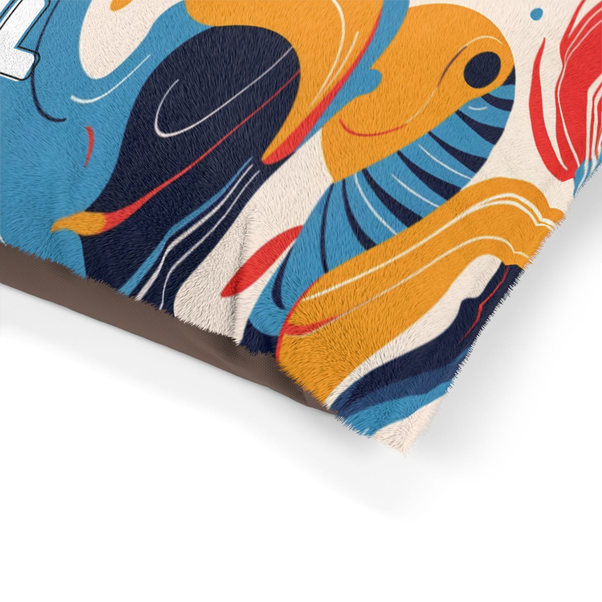 Close-up of a plush pillow corner with an African-inspired abstract design in yellow, blue, red, and black wavy shapes on a cream background. The soft, fuzzy texture stands out, with part of a brown edge visible at the bottom.