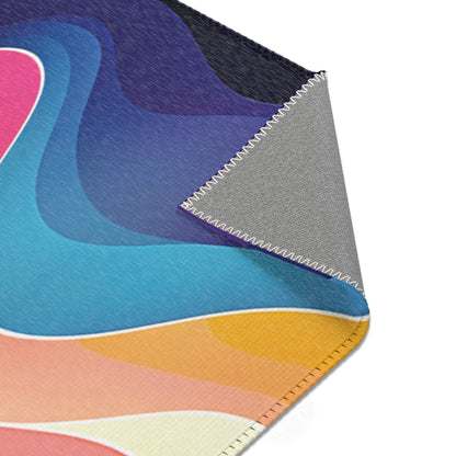 A close-up of an African-inspired fabric with a colorful abstract pattern in blue, pink, yellow, and peach tones. One corner is folded over, revealing a plain gray underside and neatly stitched zigzag edges. The surface texture is visible.