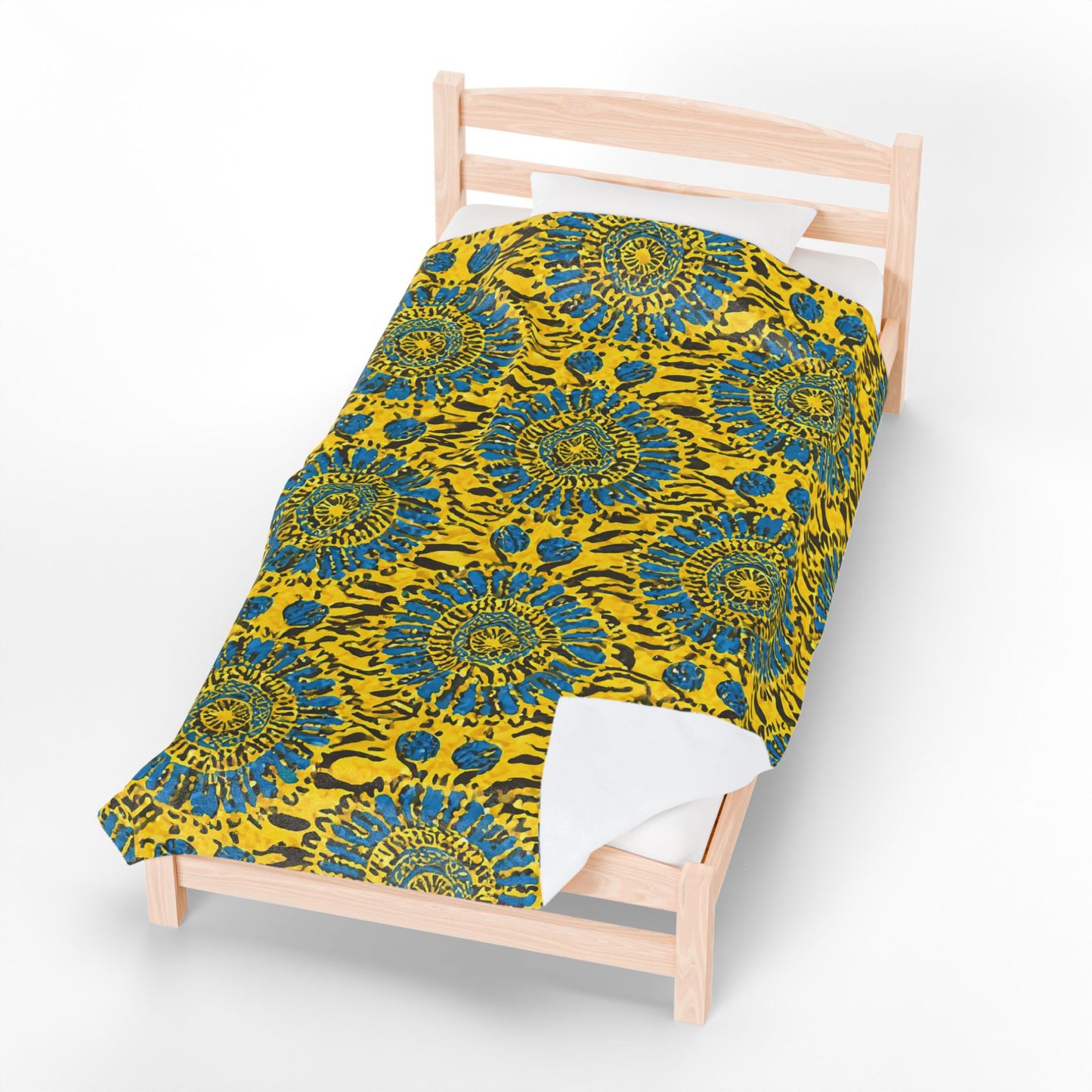 A single wooden bed with white sheets and a vibrant African-inspired blanket featuring a yellow background and bold blue and green circular floral patterns, viewed from above against a plain white backdrop.