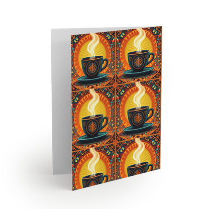 A greeting card stands open, displaying a culturally inspired design of six stylized coffee cups with swirling steam, sunbursts, and vibrant floral motifs in blue, orange, and yellow on a dark background. The inside is blank—perfect for premium stationery lovers.