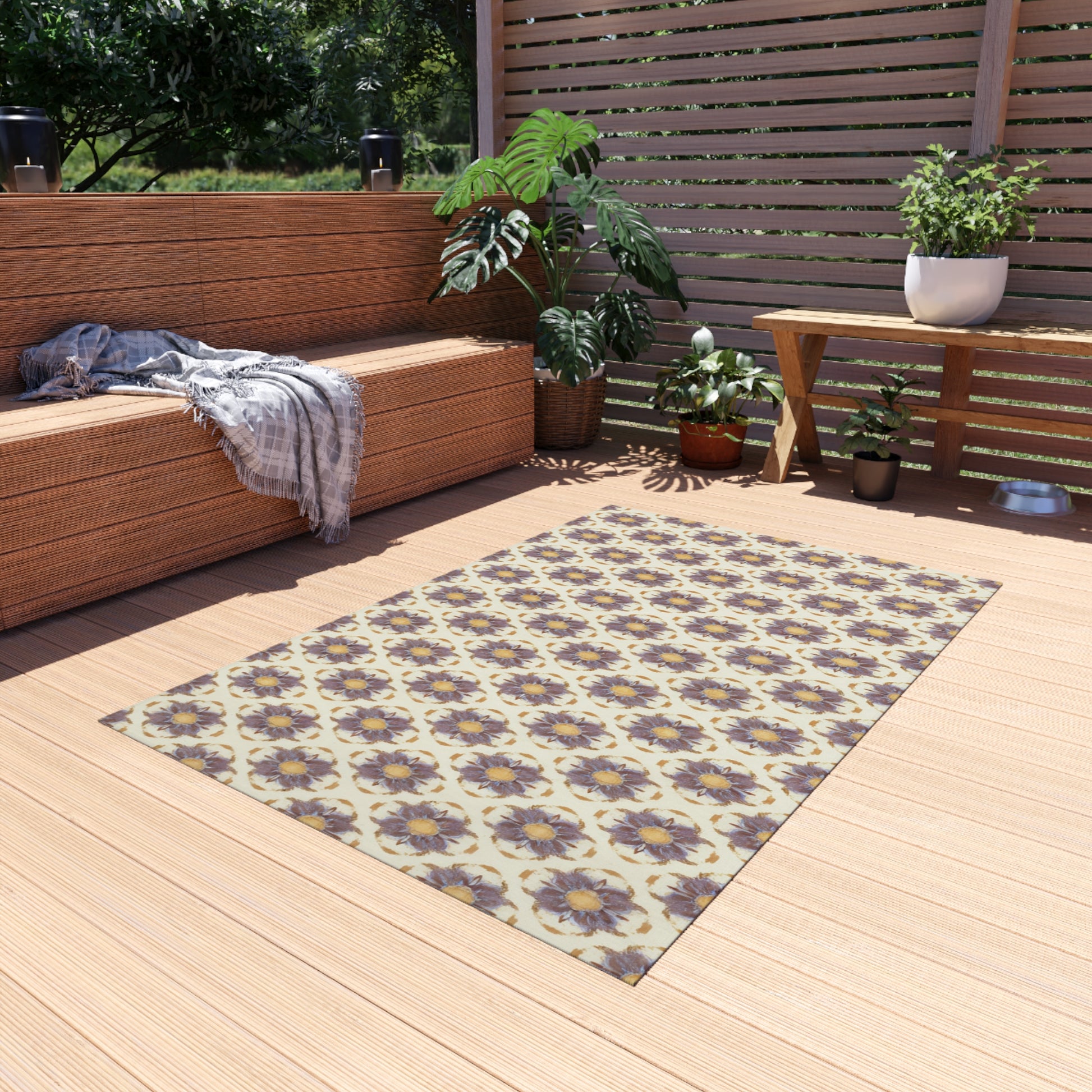 A sunlit outdoor patio with wooden flooring features an African-inspired wicker bench draped with a gray blanket, green potted plants, a wooden table with more plants, and a floral-patterned rug with purple and yellow flowers in the center.