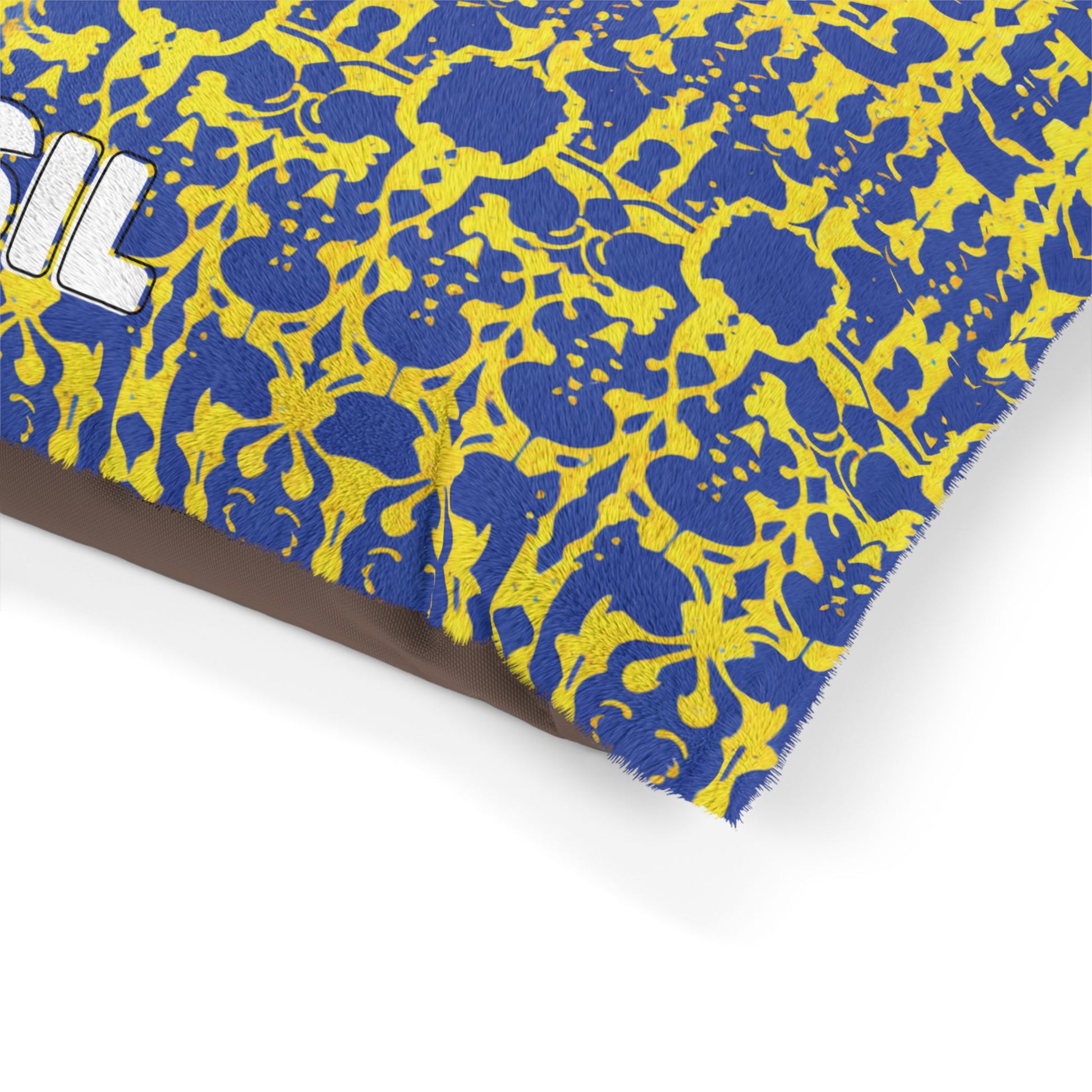 A close-up of a fabric with an African-inspired blue and yellow abstract floral pattern. The edge is frayed, and part of the word SIL in white text with black outline is visible on the left. The background is plain white.