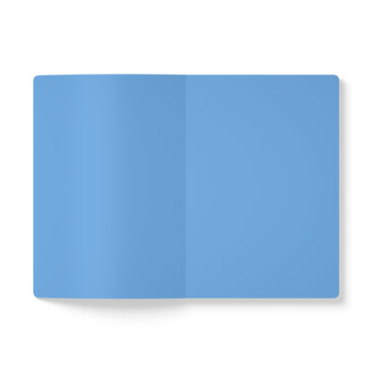 An open, blank creative journal with light blue pages is displayed against a white background. The notebook lies flat, showing a center fold and no text or markings. Shadows on the left add depth to this inviting space for daily journaling.