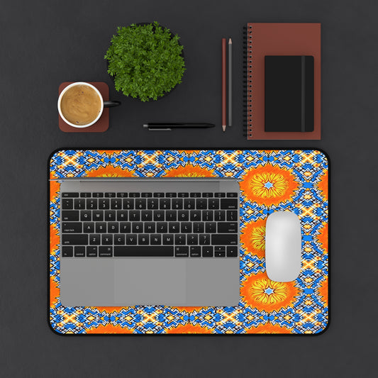 A top-down view of a workspace with a laptop and mouse on a bright, sunflower-patterned Neoprene desk mat—a colorful workspace accessory—plus a cup of coffee, small potted plant, two closed notebooks, and two pencils on a dark surface.