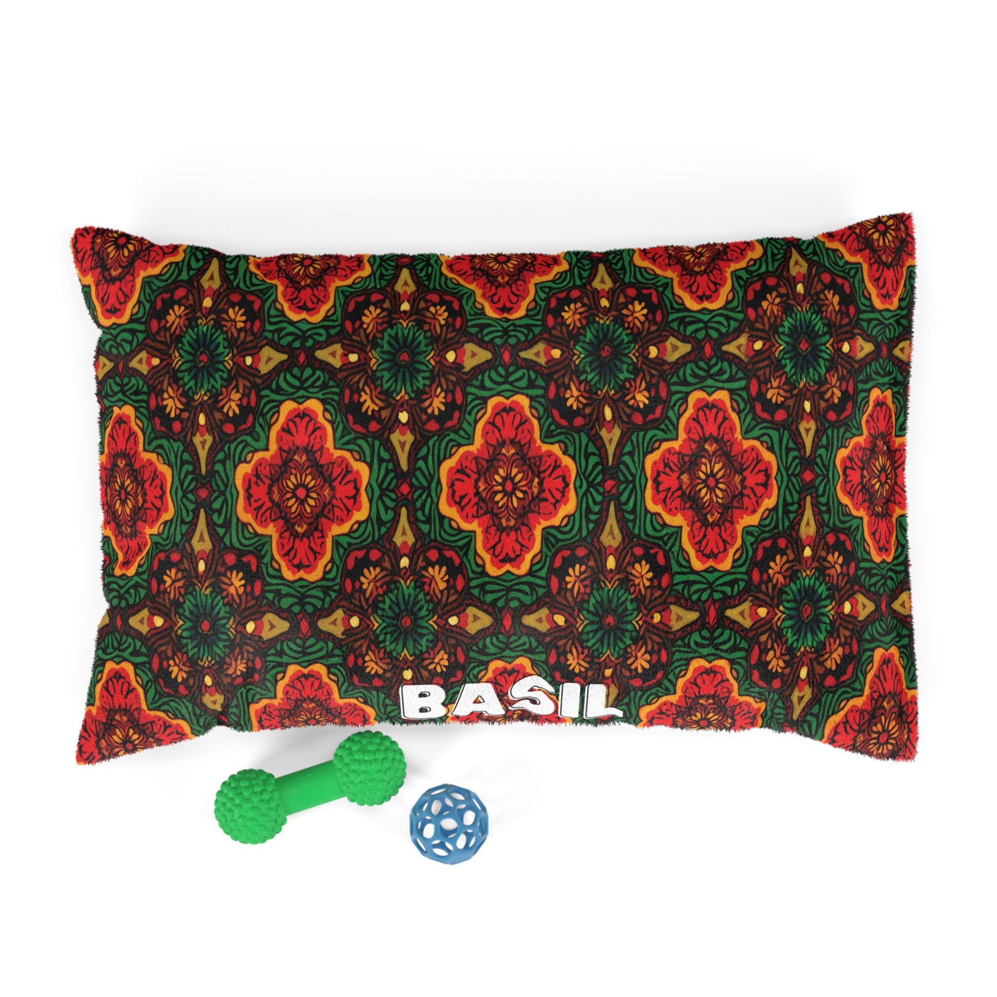 A rectangular pillow with a bold, symmetrical floral pattern in red, orange, green, and black. The name BASIL is printed in large white letters at the bottom. In front are two dog toys—perfect for personalized pet beds with durable construction.