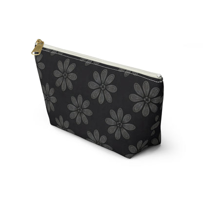 A black cosmetic travel bag with a gold zipper pull, featuring large, light gray, hand-drawn daisy-like flowers reminiscent of African-inspired patterns. This T-bottom pouch stands upright on a white background.