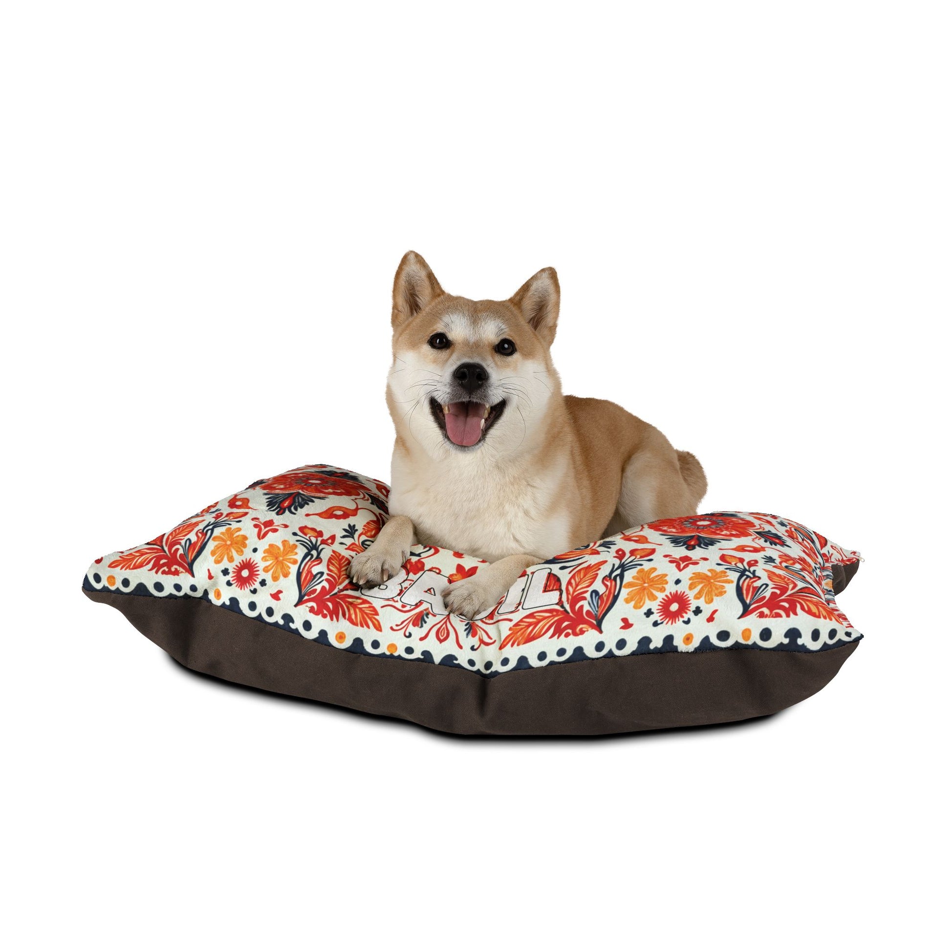 A tan and white Shiba Inu dog lies on a colorful, African-inspired floral-patterned cushion bed with a brown base, looking forward with its mouth open and tongue out, against a plain white background.
