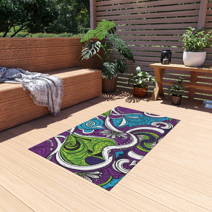 A colorful rectangular polyester chenille rug with swirling abstract patterns in purple, green, blue, and white lies on a light wooden deck. Potted plants and a bench add comfort to this cozy outdoor space featuring weather-resistant rugs.