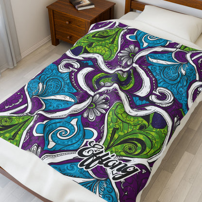 A neatly made bed features an African-inspired blanket with swirling, abstract patterns in purple, blue, and green. The word Effiang is written in stylized script on the corner. A wooden nightstand and lamp are nearby.