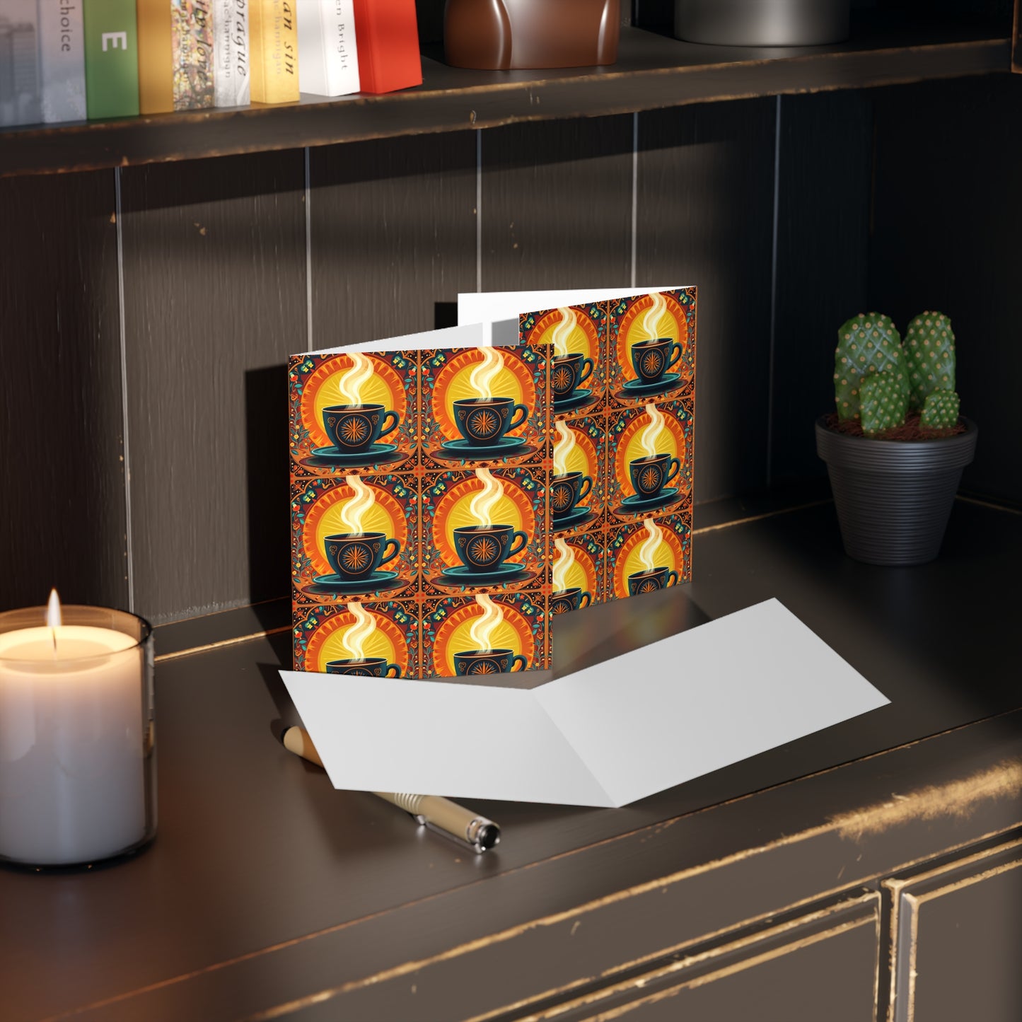 A blank card and pen rest on a dark wooden shelf, next to a lit candle and small potted cactus. Behind them, a card with a culturally inspired design of steaming coffee cups adds vibrancy, while books are stacked on the upper shelf.